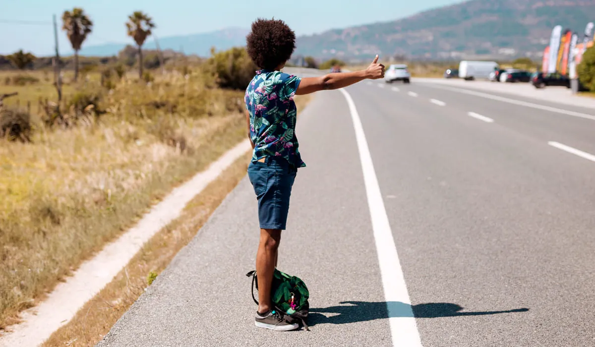 Homme faisant de l'auto-stop aux abords d'une route Homme faisant de l'auto-stop aux abords d'une route